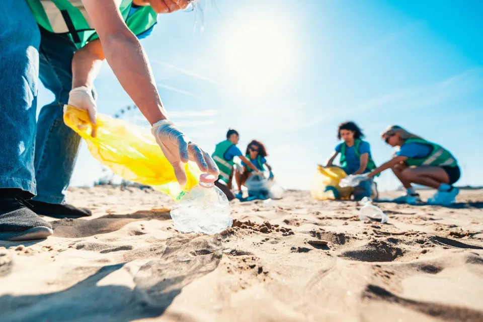 People at beach on sunny day doing clean-up of plastic bottles and other trash.